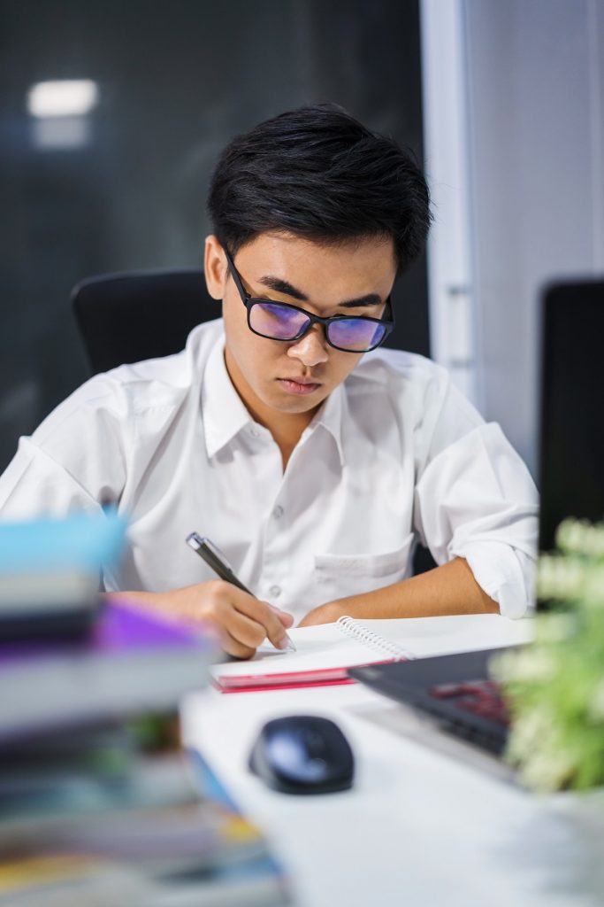 young man studying and writing on notebook with laptop