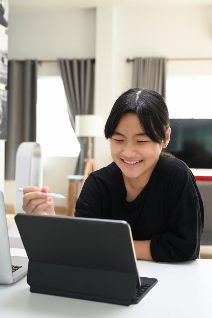 Portrait of young Asian girl video conference with teacher on tablet computer at home